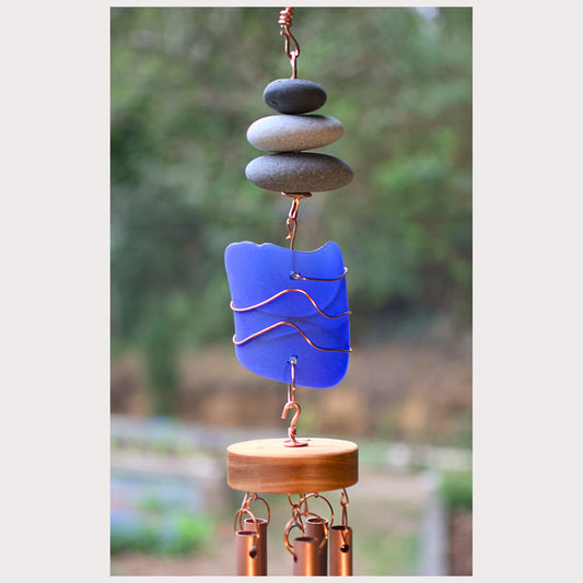 Decorative wind chime with blue glass piece and stones on a blurred natural background