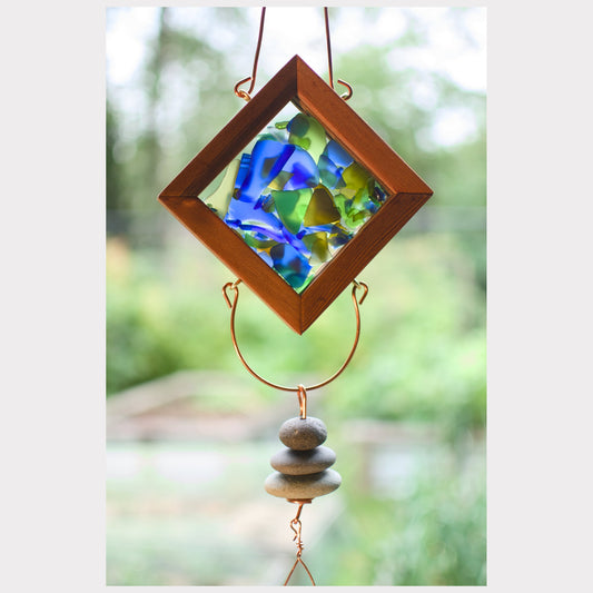 Decorative hanging ornament with blue glass pieces and pebbles against a blurred natural background