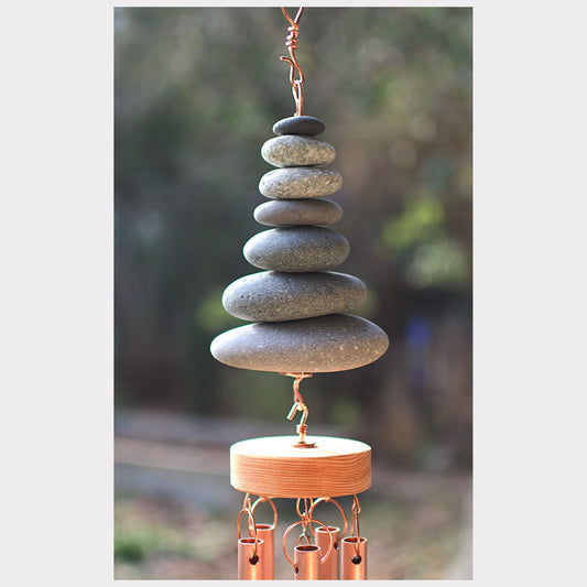 Stacked stone wind chime with copper accents against a blurred natural background