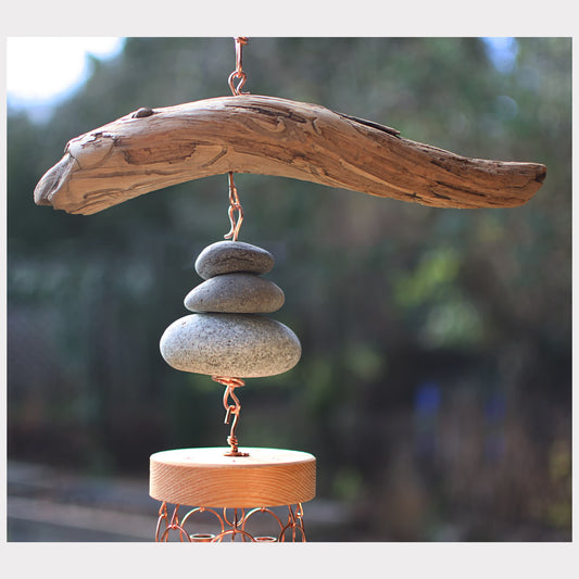 Decorative hanging sculpture with stacked stones and driftwood against a blurred natural background