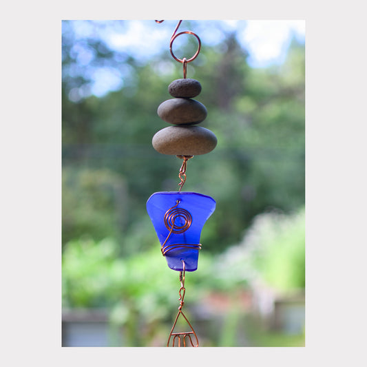 Decorative hanging with stones and a blue glass piece against a blurred green background