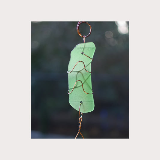 Green glass ornament with copper wire on a blurred natural background