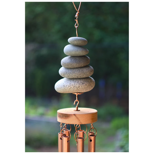 Decorative wind chime with stacked stones and copper tubes against a blurred green background