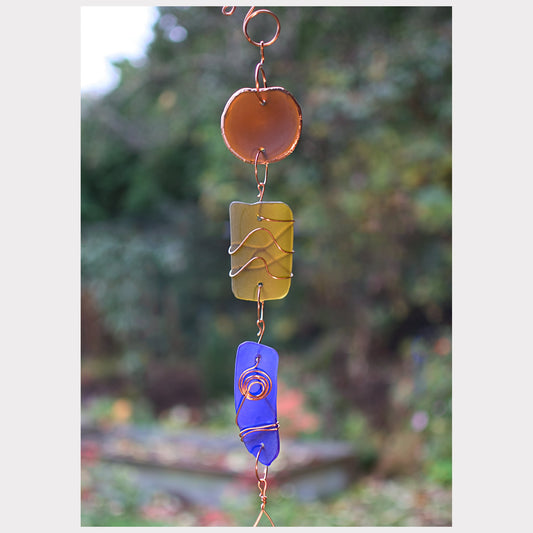 Decorative wind chime with colorful glass panels against a blurred natural background