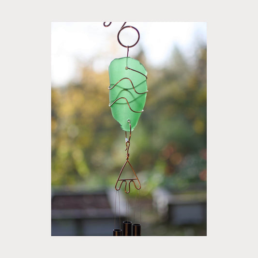 Decorative green glass wind chime with metal components against a blurred natural background