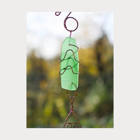 Decorative green glass hanging ornament with wirework against a blurred natural background