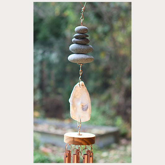Decorative wind chime with stacked stones and a shell against a blurred natural background