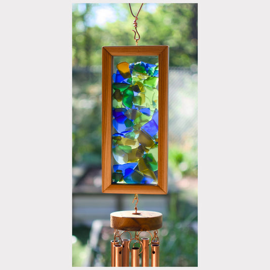 Decorative wind chime with colorful glass panels and wooden frame against a blurred green outdoor background.
