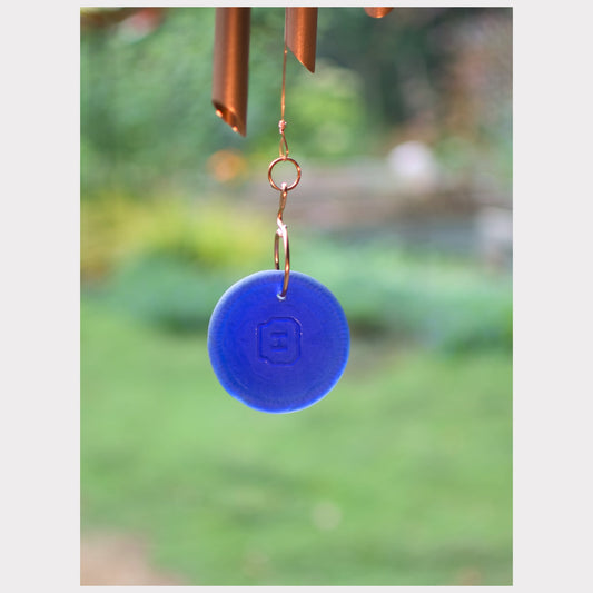 Blue wind chime disc with a blurred garden background