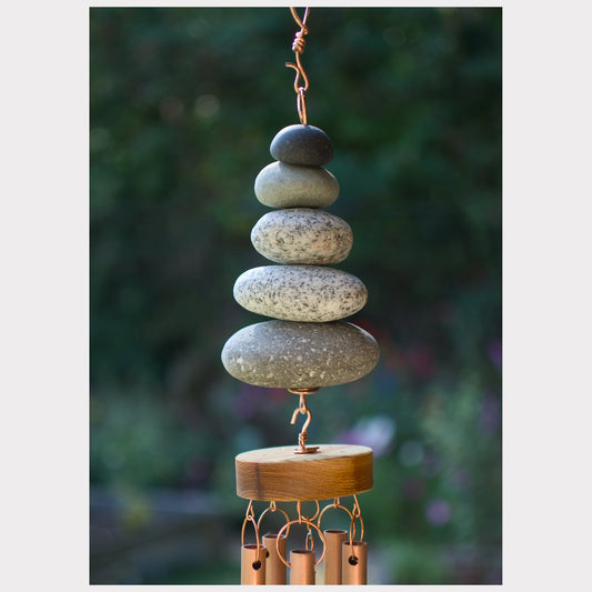 Stacked stone wind chime with wooden base against a blurred natural background