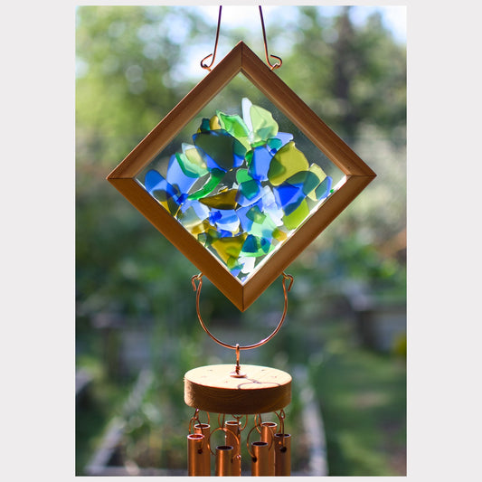 Decorative wind chime with stained glass panel and wooden base against a blurred green background