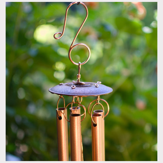 Detail, top of a handcrafted copper wind chime featuring an antiqued metal chime holder.