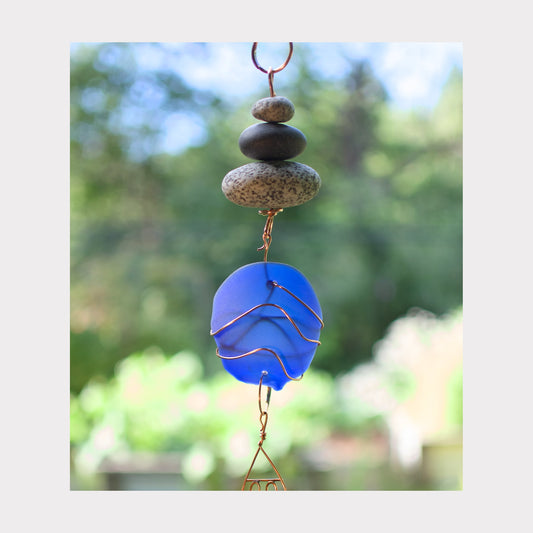 Decorative hanging with blue glass piece and stones against a blurred natural background