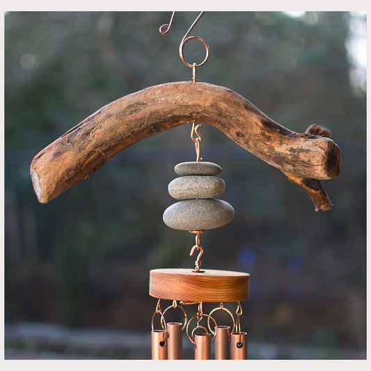 Wooden wind chime with stones and metal components against a blurred natural background