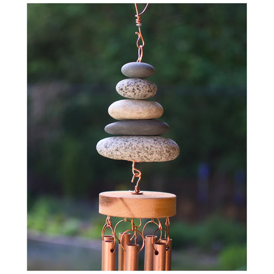 Decorative wind chime with stacked stones and copper tubes against a blurred natural background