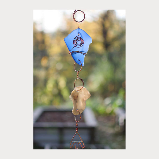 Decorative wind chime with blue and beige elements against a blurred natural background