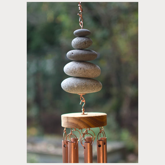Decorative wind chime with stacked stones and copper tubes against a blurred natural background