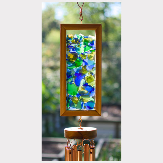 Decorative wind chime with colorful glass panels and wooden frame against a blurred natural background