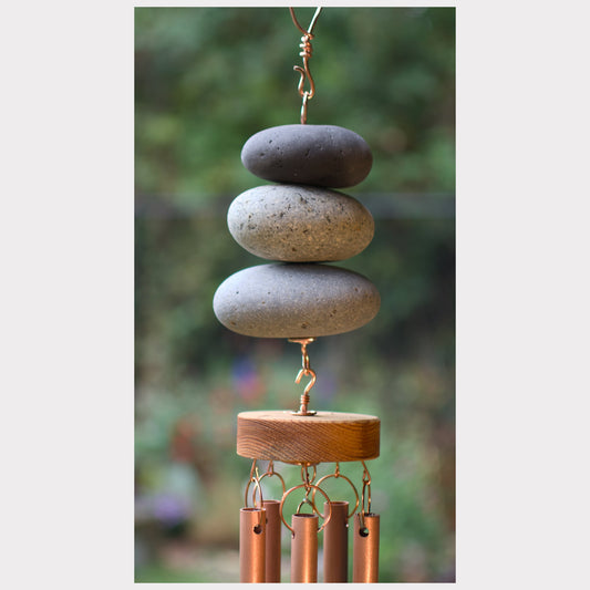 Decorative wind chime with stacked stones and copper tubes against a blurred natural background