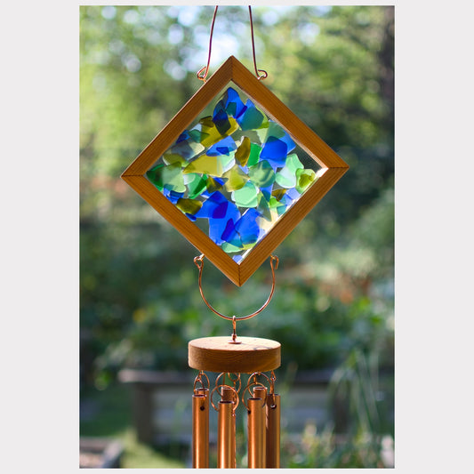 Decorative wind chime with colorful glass panels and copper tubes against a blurred green background