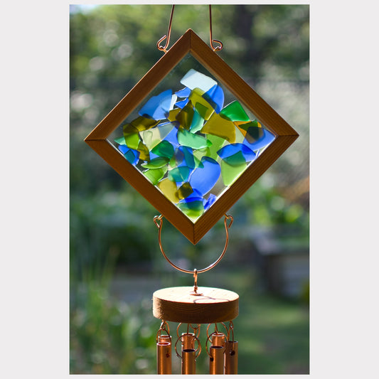 Decorative wind chime with colorful glass panels and brass components against a blurred green outdoor background.