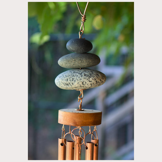 Decorative wind chime with stacked stones and wooden base against a blurred natural background
