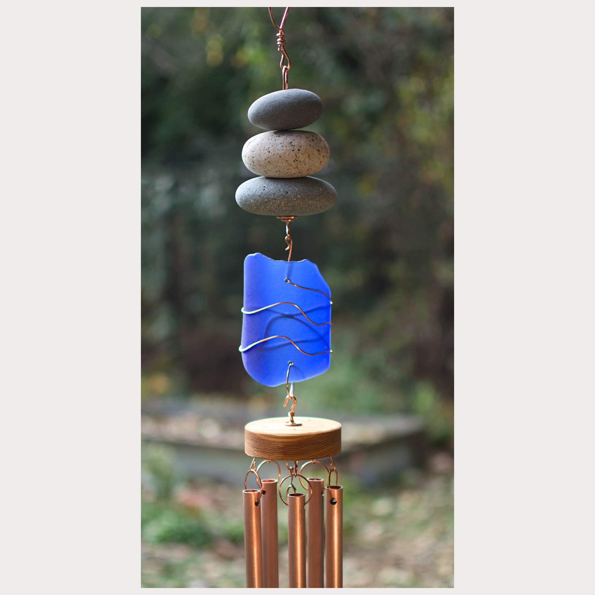 Decorative wind chime with blue glass panel and pebble top on a blurred natural background