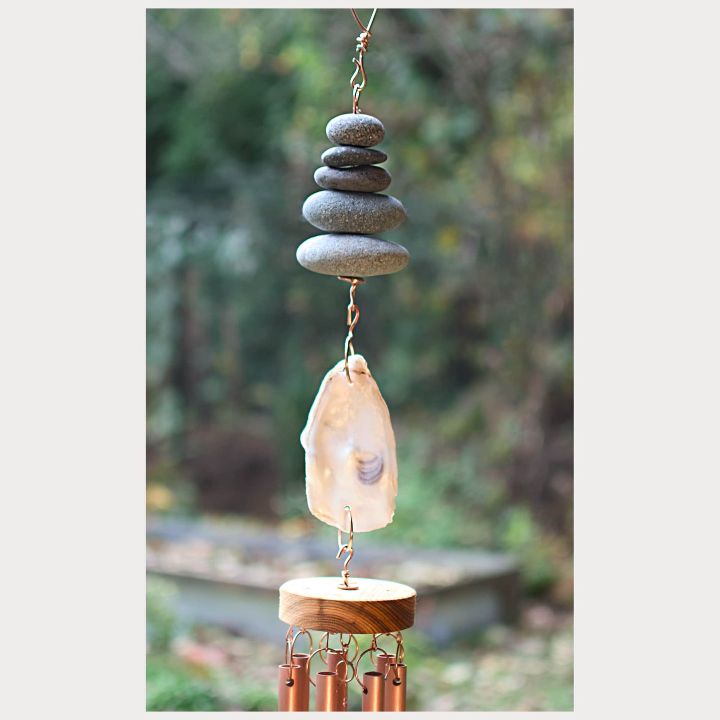 Decorative wind chime with stacked stones and a shell against a blurred natural background