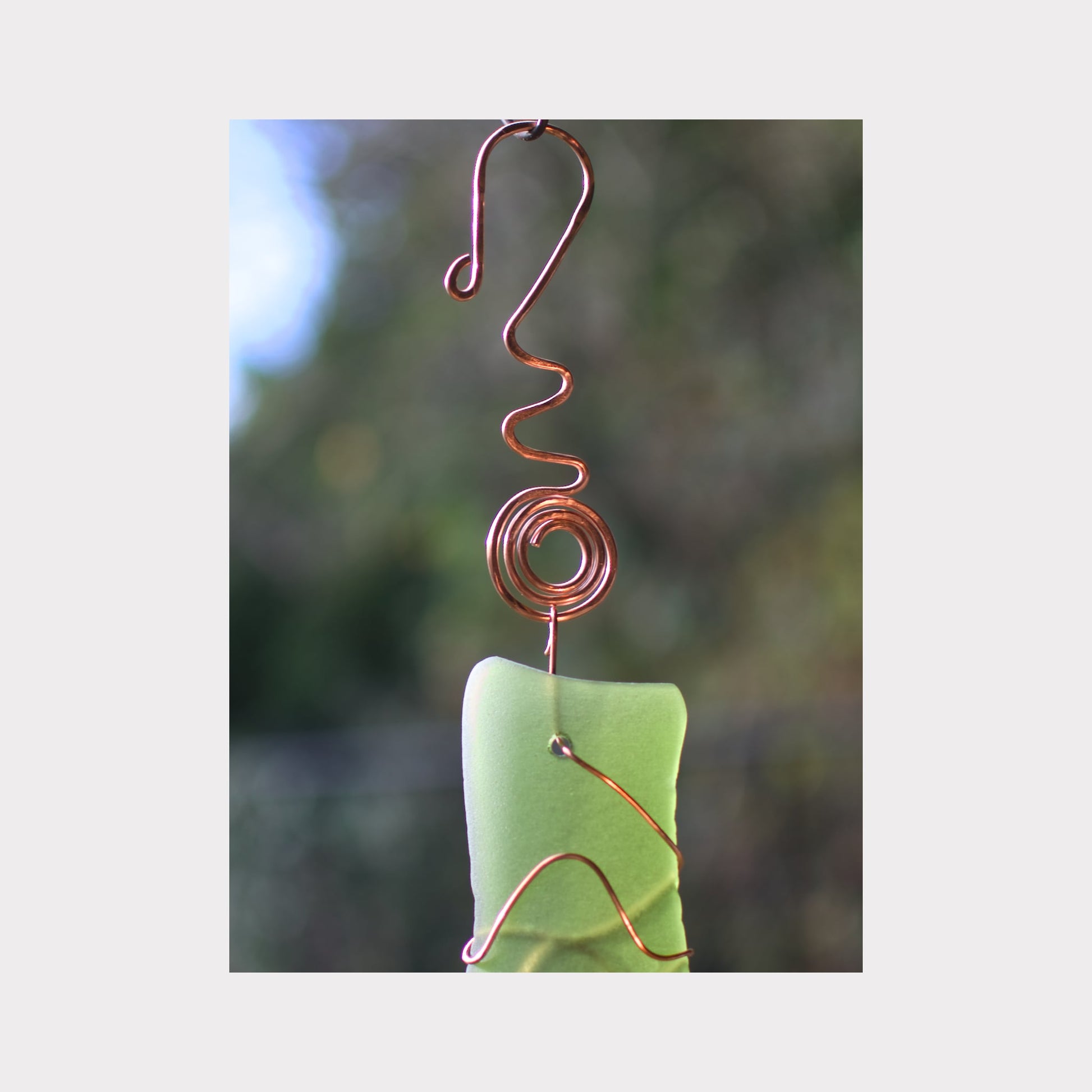 Decorative hanging ornament with green sea glass and copper wire on a blurred natural background