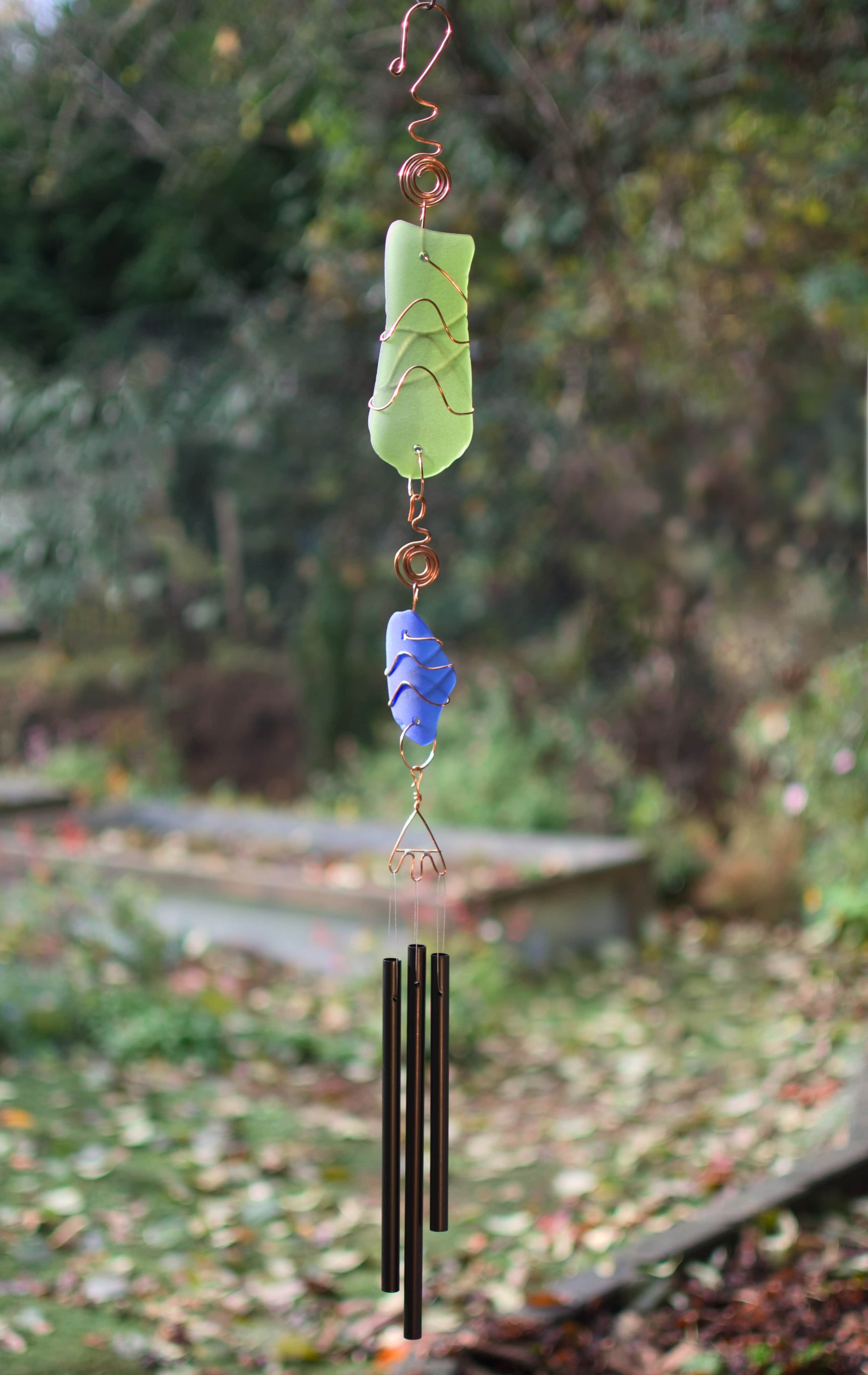 Decorative wind chime with green and blue glass elements against a natural background