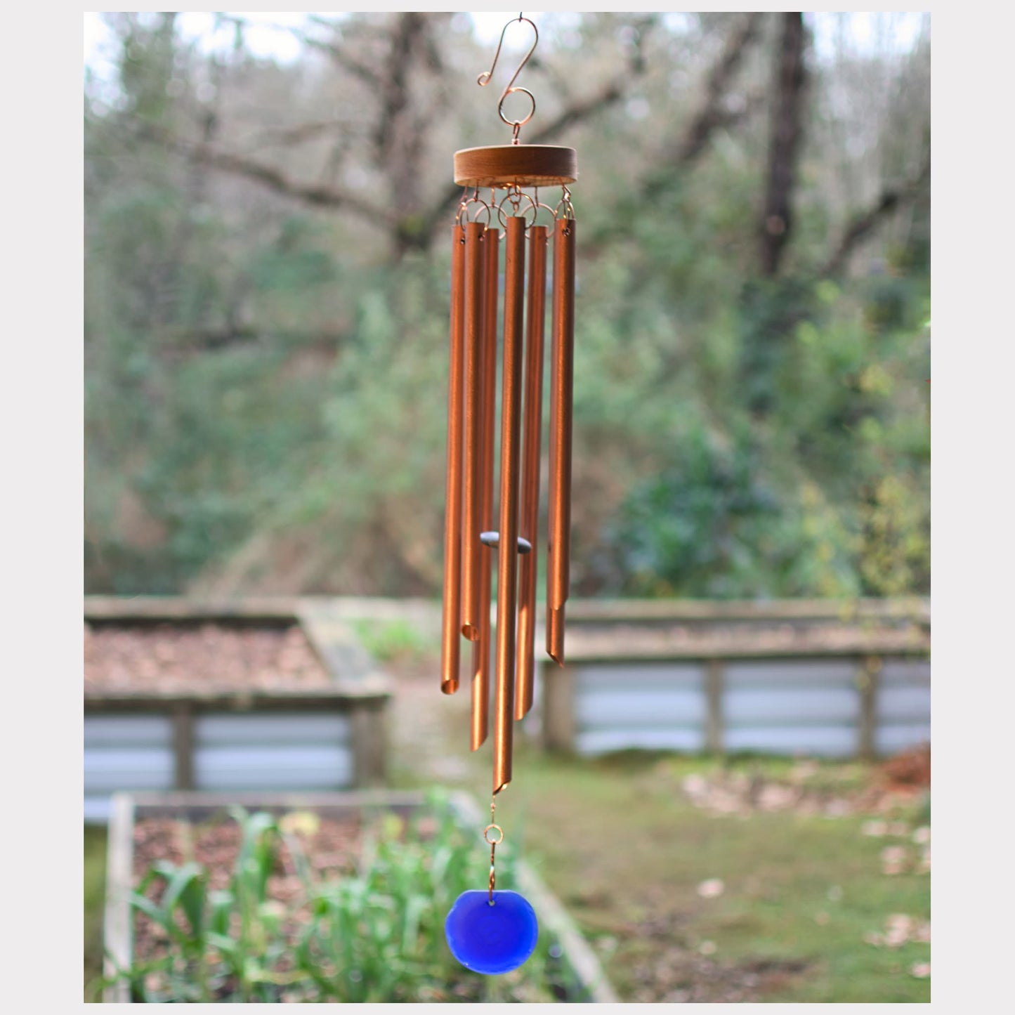 Copper wind chime with a blue glass windsail in a garden setting