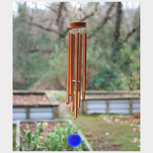 Copper wind chime with a blue glass windsail in a garden setting