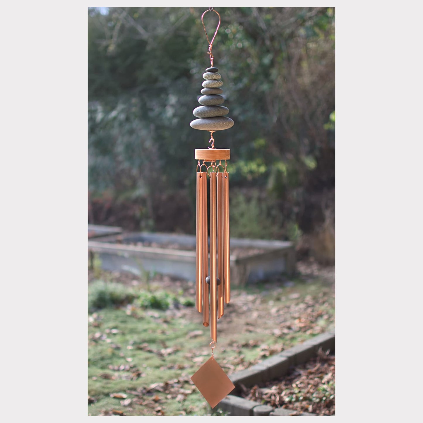 Decorative wind chime with stones and copper elements against a natural background