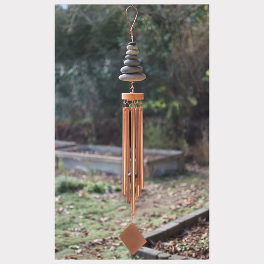 Decorative wind chime with stones and copper elements against a natural background