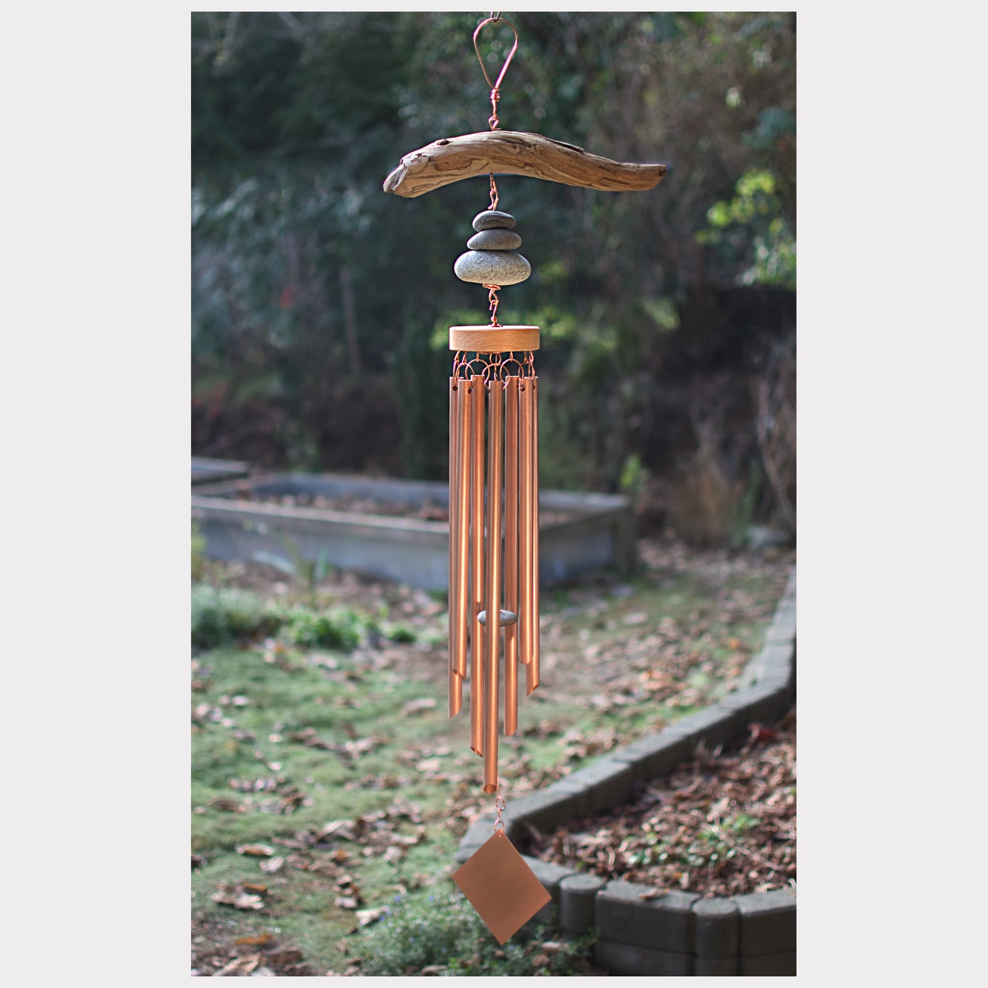 Decorative wind chime with stones and copper tubes hanging outdoors.
