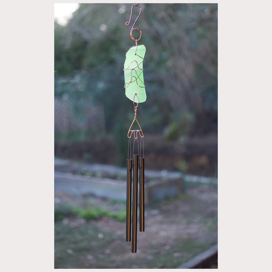 Decorative wind chime with a green glass piece against a blurred natural background