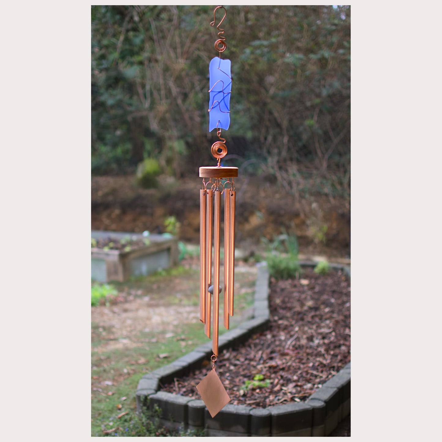 Copper wind chime with blue hanging in a garden setting