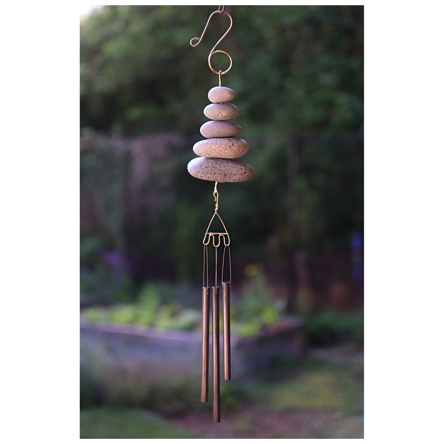 Decorative wind chime with stacked stones and brass tubes against a garden background