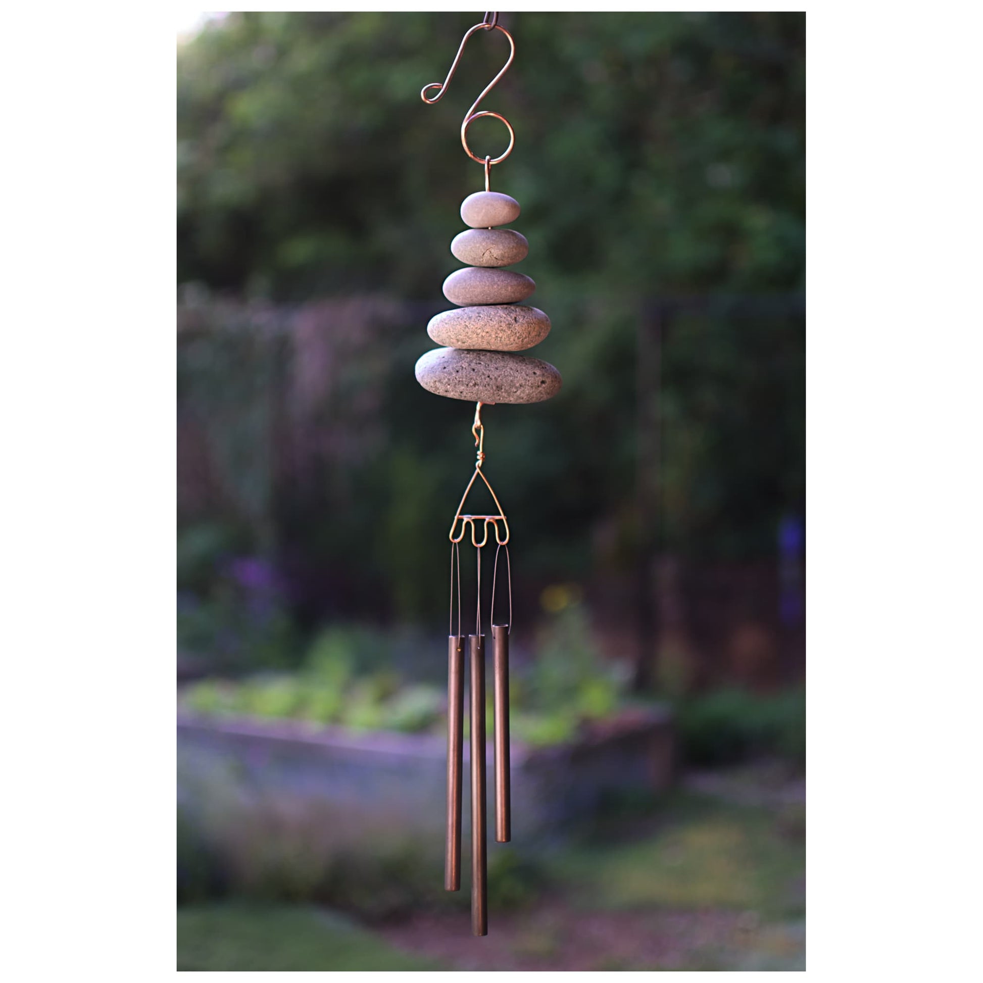 Decorative wind chime with stacked stones and brass tubes against a garden background