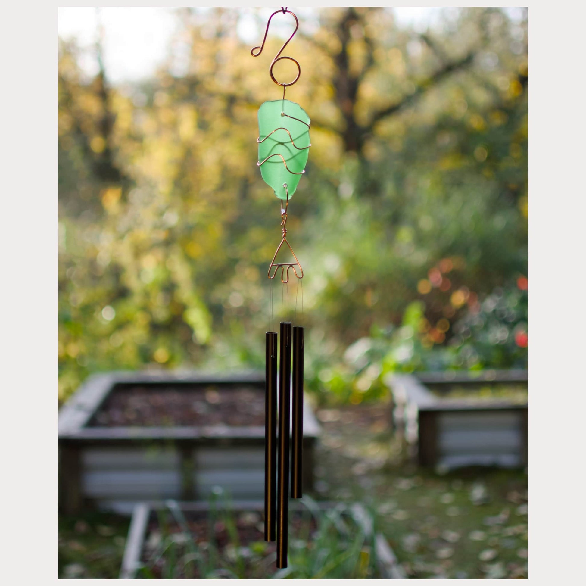 Decorative wind chime with a green glass piece against a blurred garden background