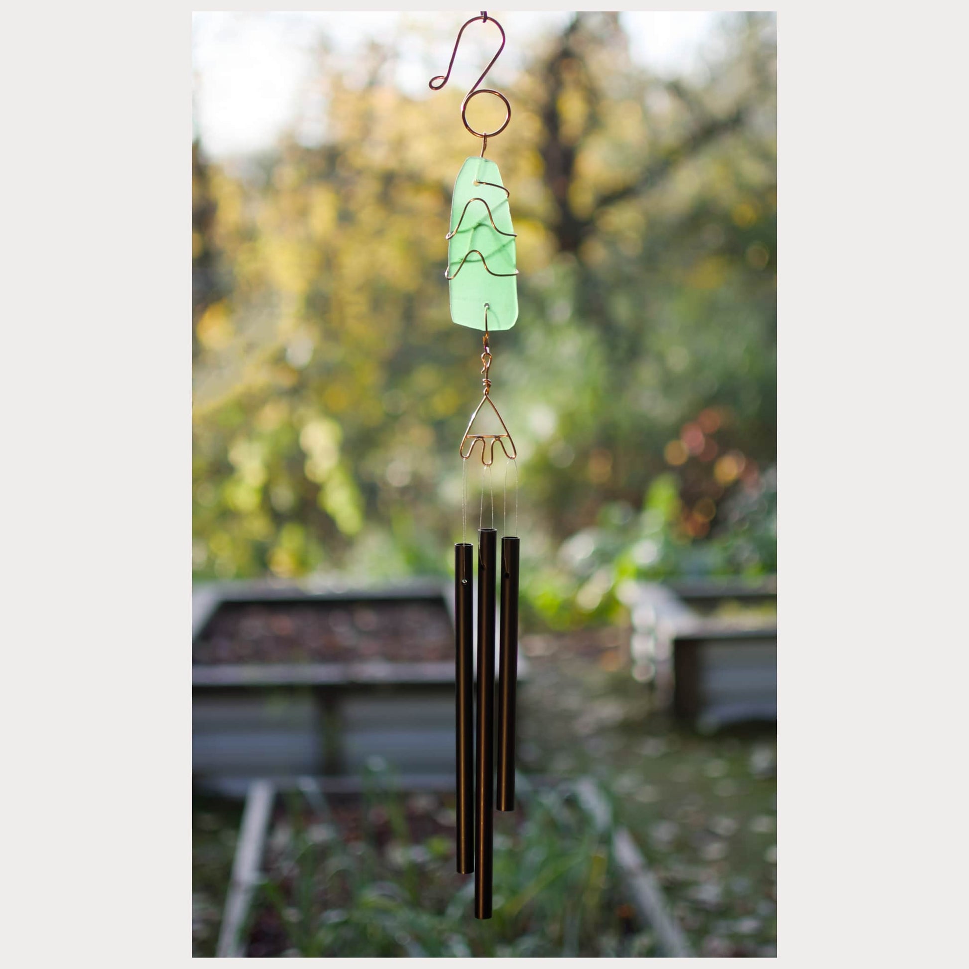 Decorative wind chime with a green top and black rods against a blurred garden background