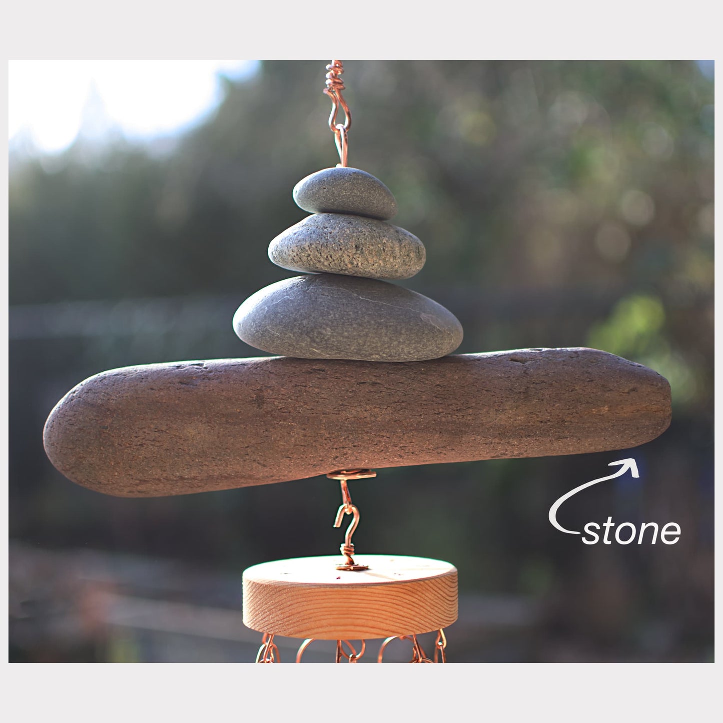Decorative hanging sculpture with stacked stones and a wooden base against a blurred natural background