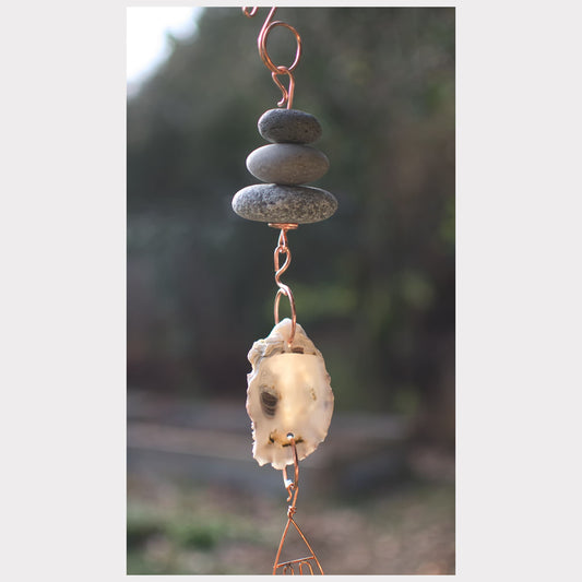 Decorative hanging with stones and a shell against a blurred natural background