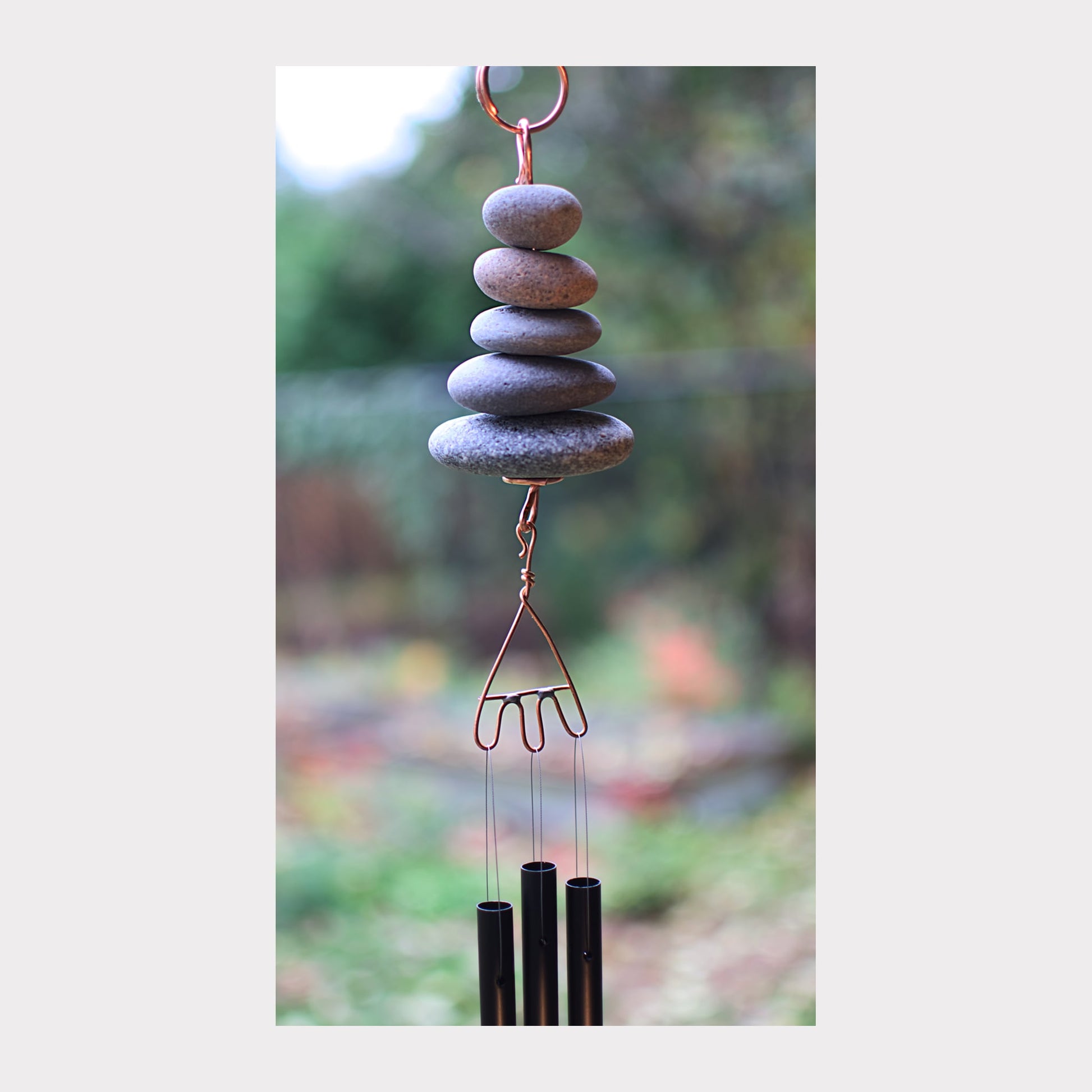 Decorative wind chime with stacked stones and metal components against a blurred natural background