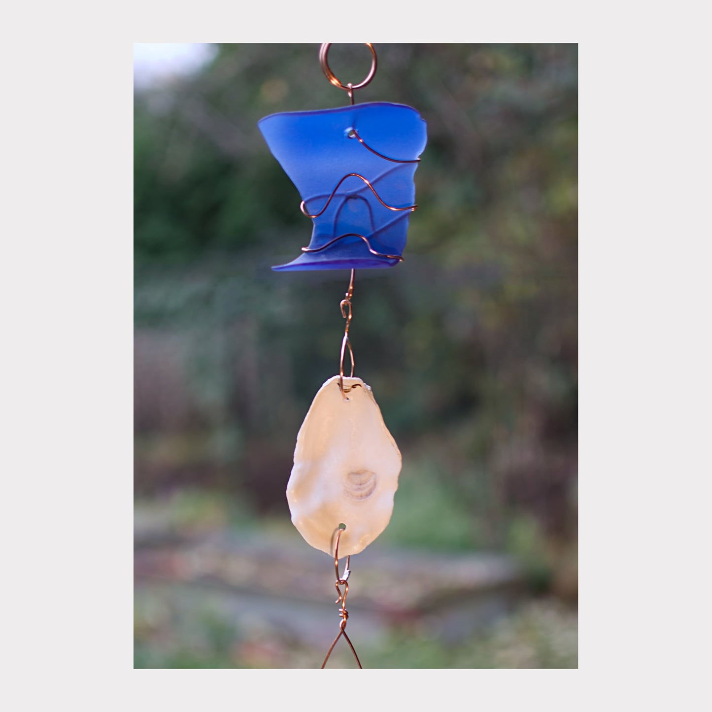 Decorative hanging with blue glass piece and beige stone against a blurred natural background