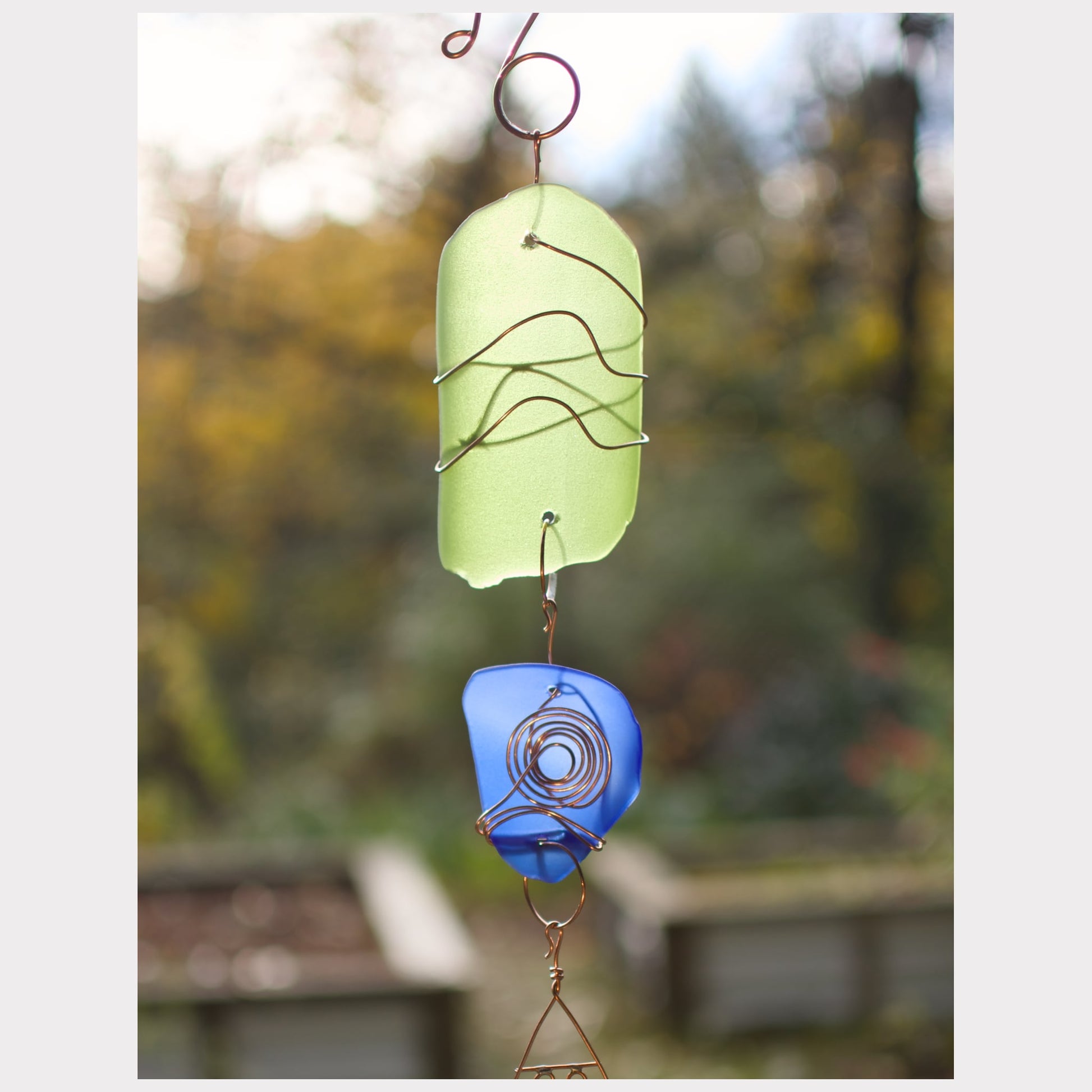 Decorative hanging with green and blue glass pieces against a blurred natural background