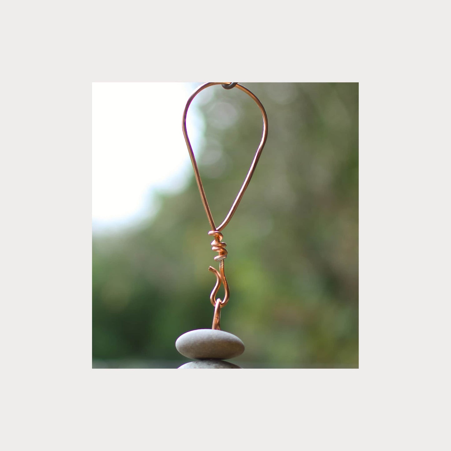 Copper wire heart-shaped ornament on a stone with a blurred natural background