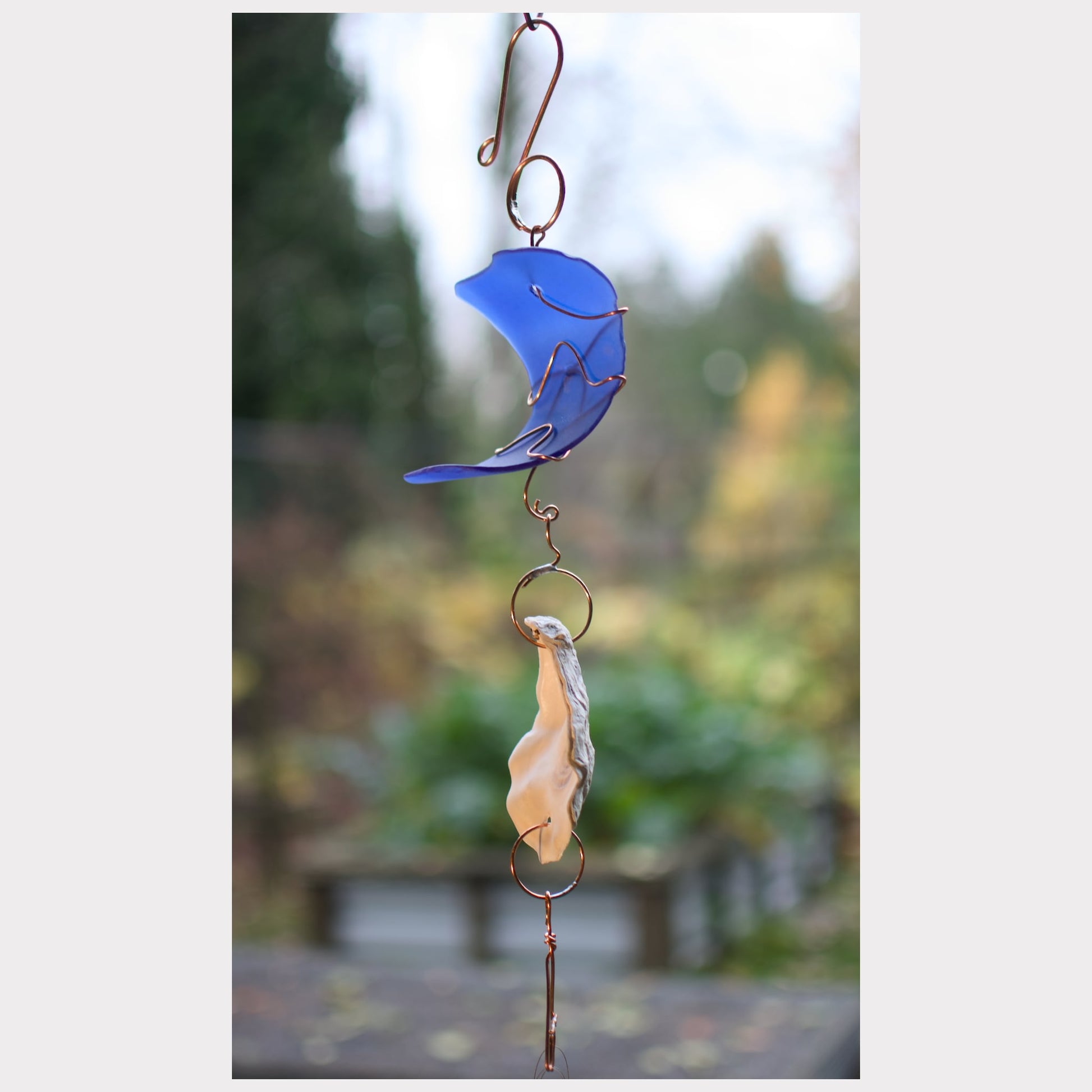 Decorative wind chime with blue and beige elements against a blurred natural background