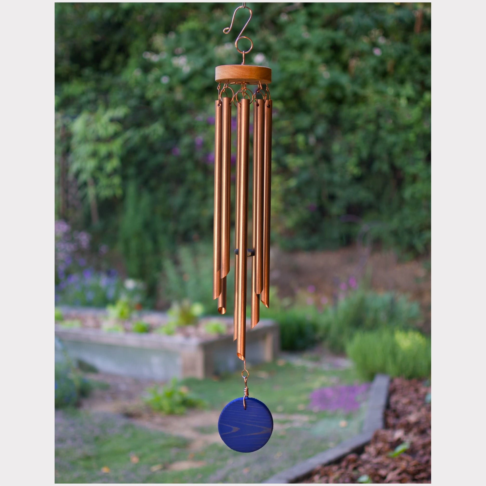 Copper wind chime with blue disc hanging in a garden