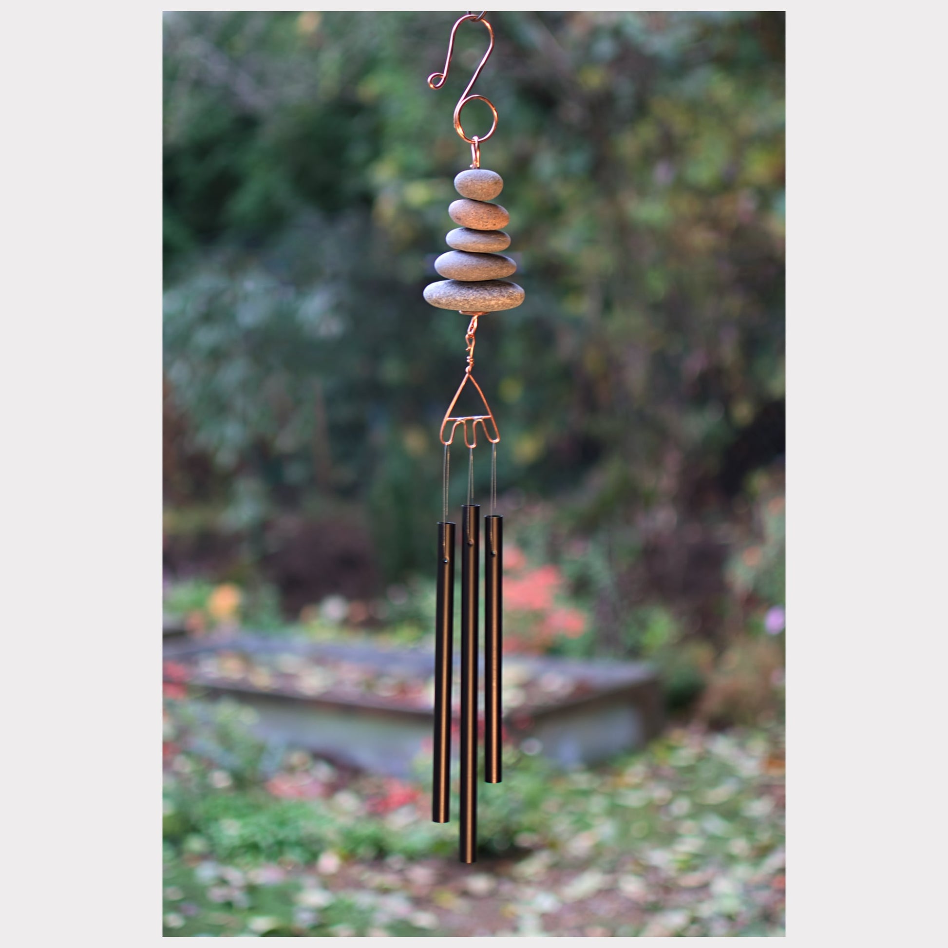 Decorative wind chime with stones and metal tubes against a garden background